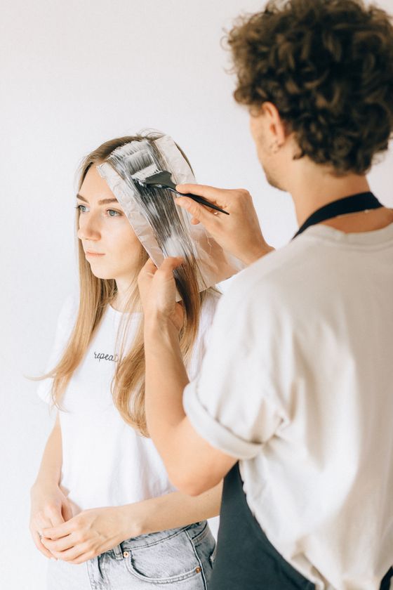 Fryzjer nakłada rozjaśniacz na długie blond włosy